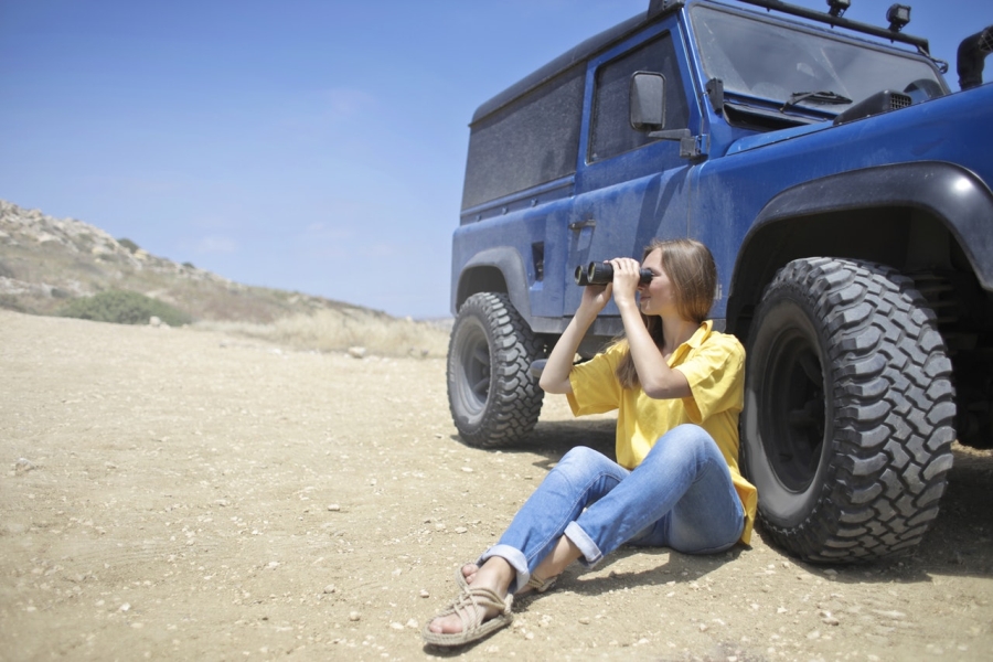 Žena sedící na suché zemi pozoruje krajinu dalekohledem